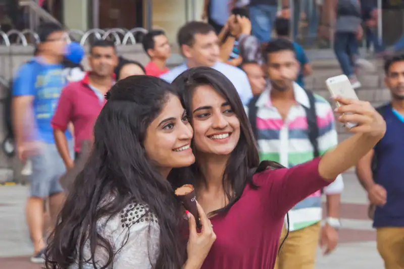 Two young women smiling and taking a selfie together on a street in Kuala Lumpur