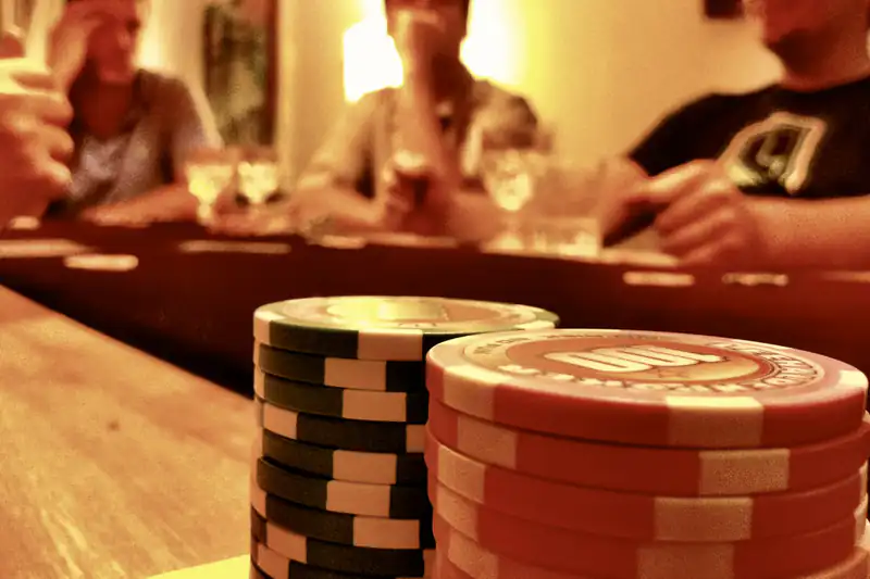 Stacks of casino chips on a table with friends playing in warm light