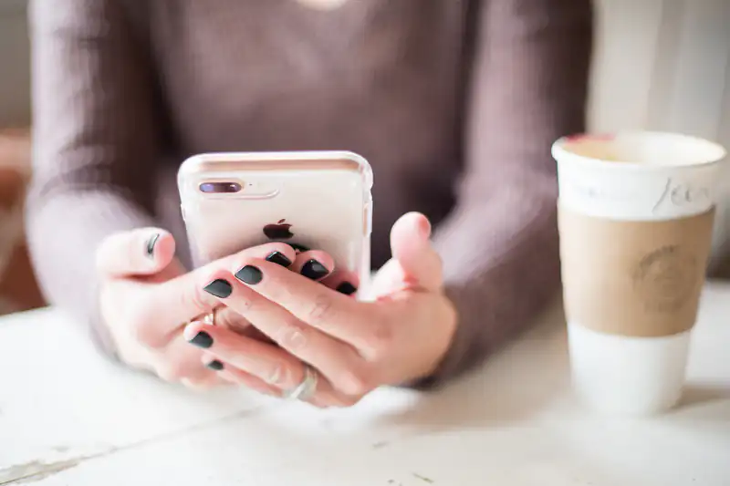 Close-up of a woman holding an iPhone beside a cup of coffee