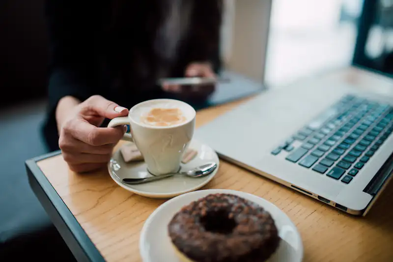 Woman using her smartphone beside a coffee, a donut and a laptop